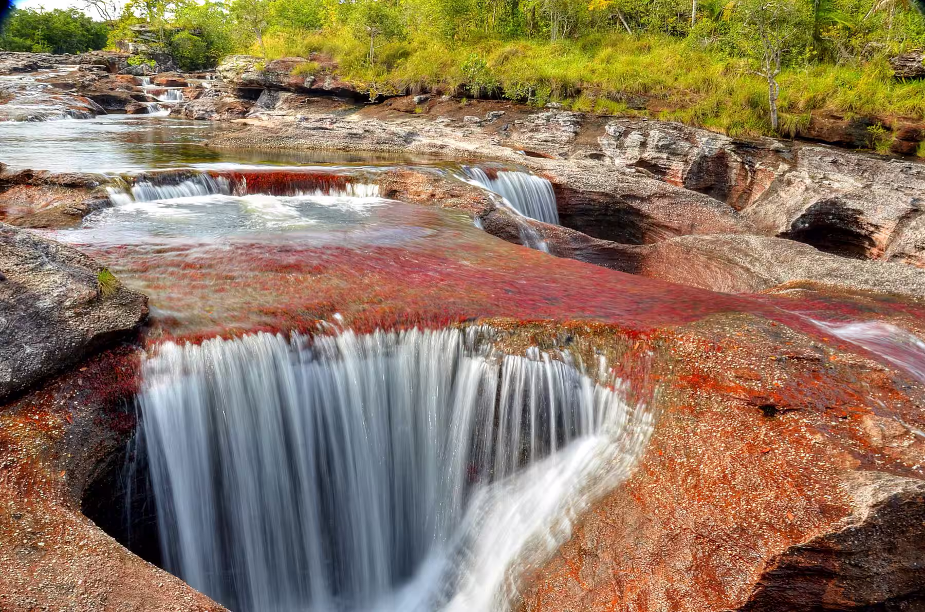 Pozo Los Ocho en Caño Cristales, con el agua cayendo sobre roca roja